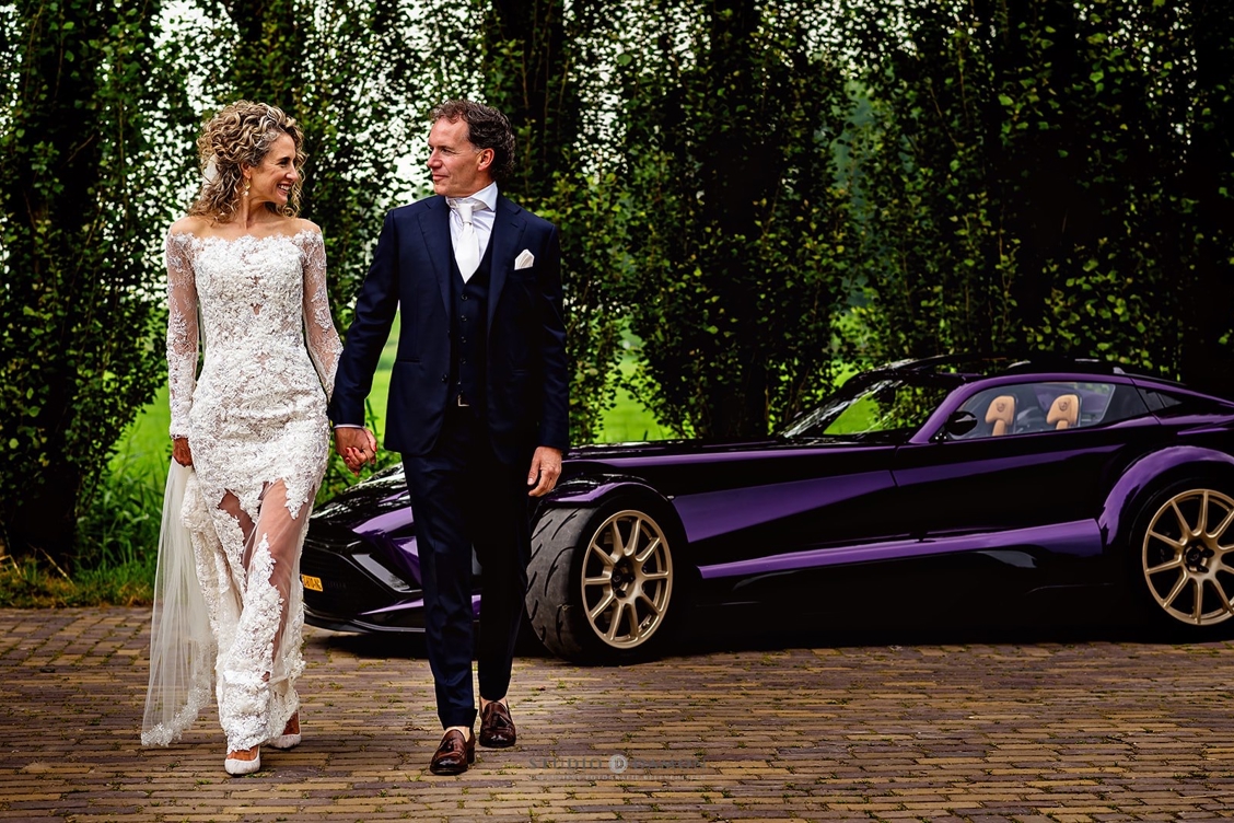 “Steffie & Leonard hand in hand bij een luxe trouwauto – onderdeel van hun high end wedding, georganiseerd door een exclusieve weddingplanner