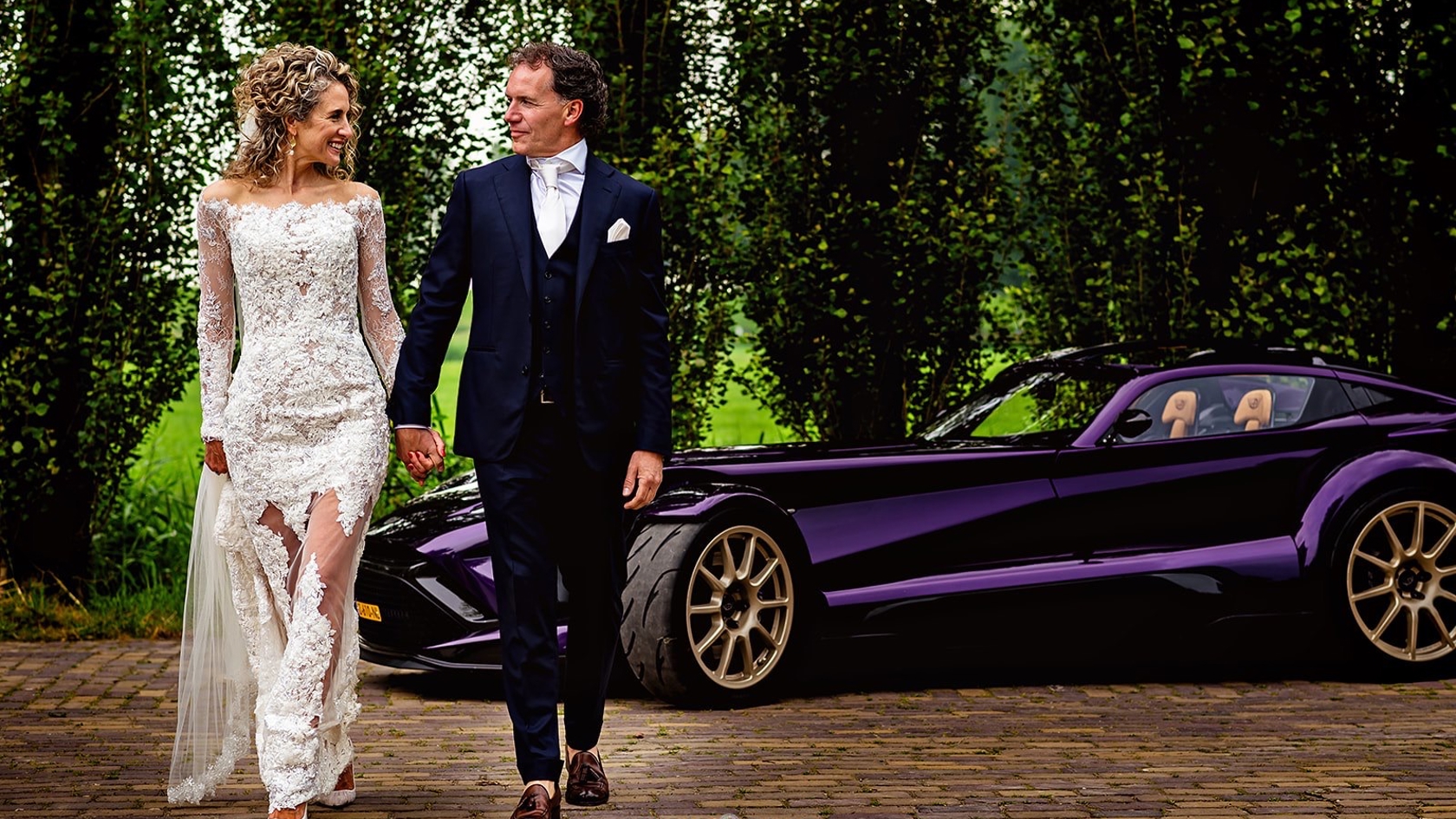 “Steffie & Leonard hand in hand bij een luxe trouwauto – onderdeel van hun high end wedding, georganiseerd door een exclusieve weddingplanner