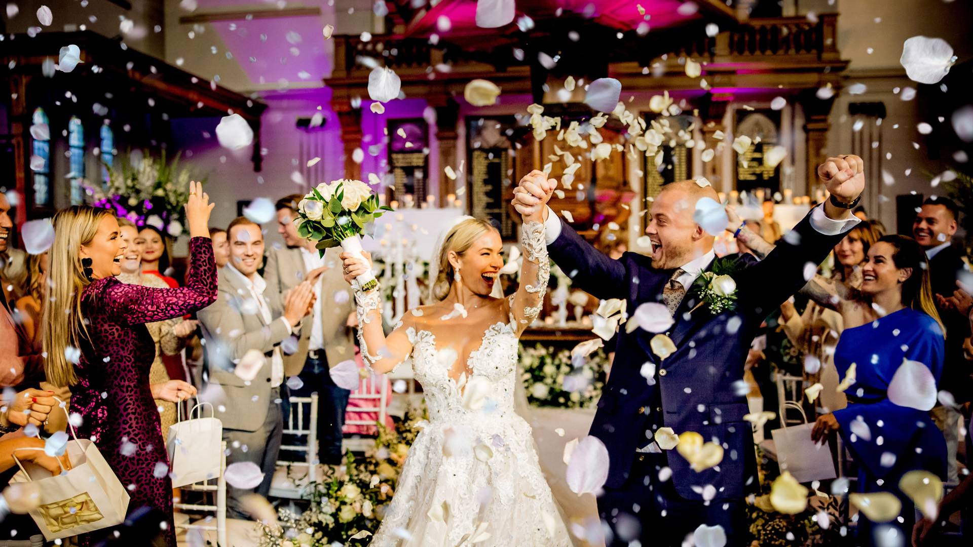 Stralend bruidspaar viert hun bruiloft omringd door vrienden en bloemenconfetti in een feestelijk versierde trouwlocatie. - Wiesje Wedding Planner